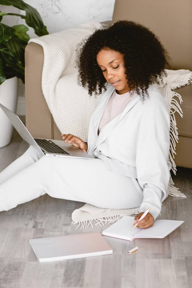 Black woman blogging between laptop and writing notes in a notebook