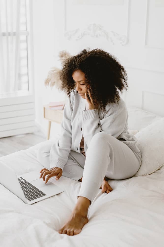 Black woman working on her blog and on the phone at the same time in bed.