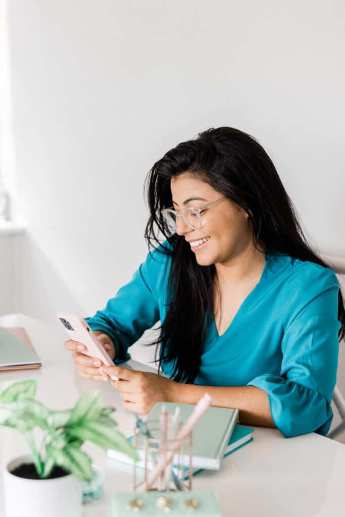 Woman laughing on her phone as she types next to her laptop 