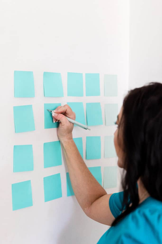 Woman writing on teal post it notes on her wall making her business plan 