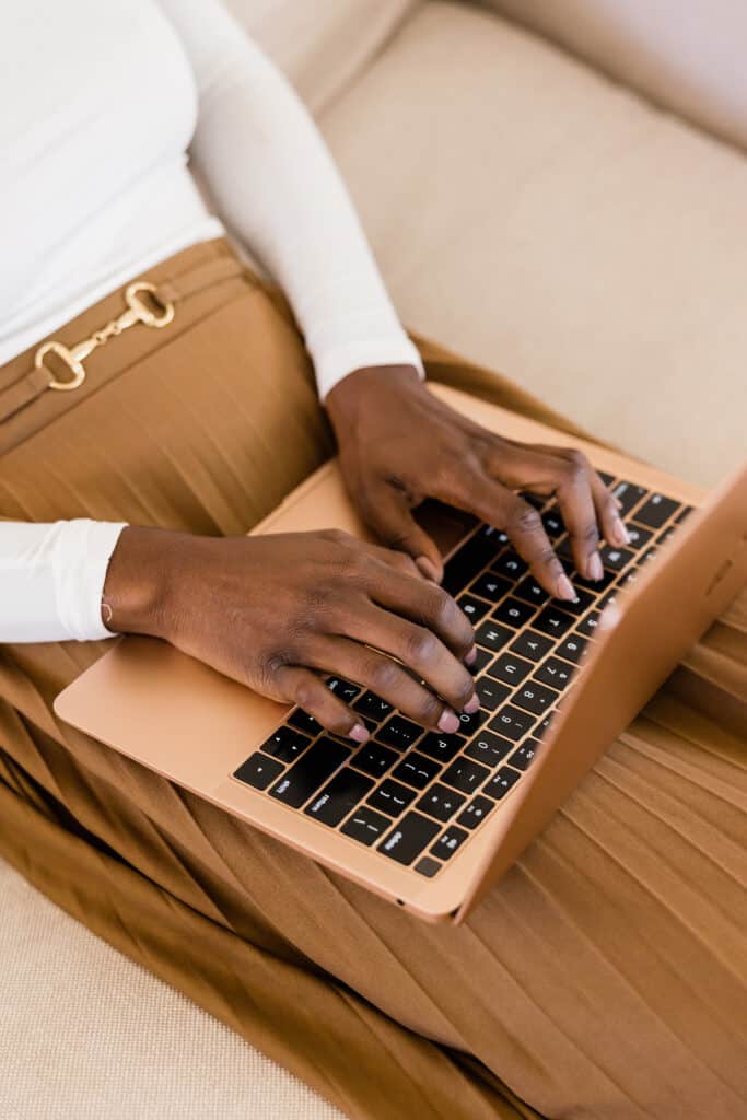 Black woman using a rose gold laptop to write her blog posts 